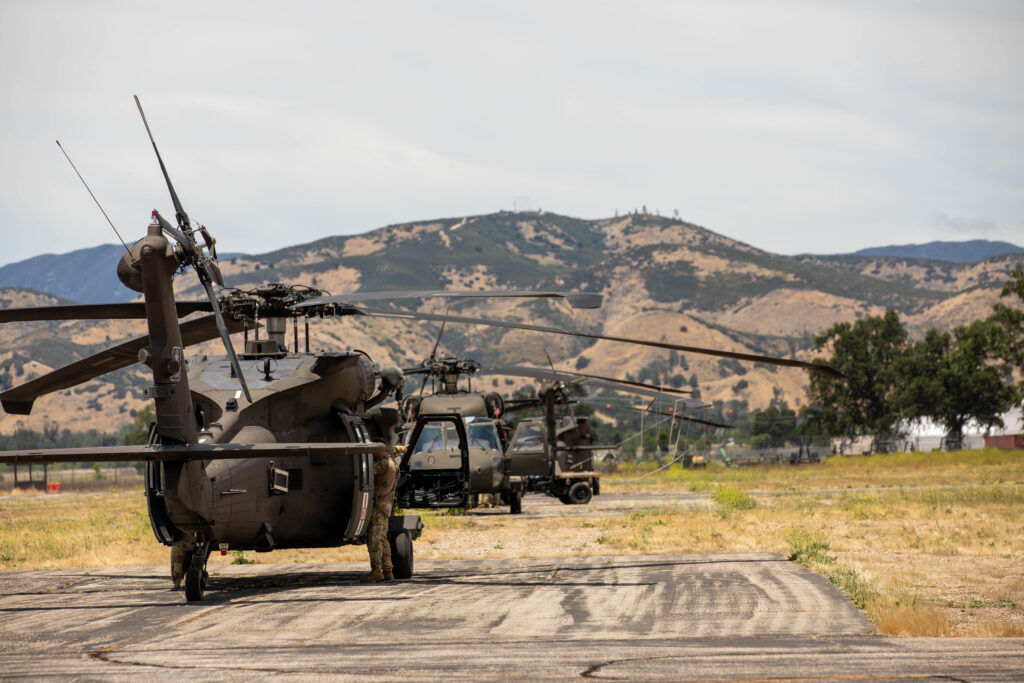 Black Hawks sit on the tarmac in a desert landscape.
