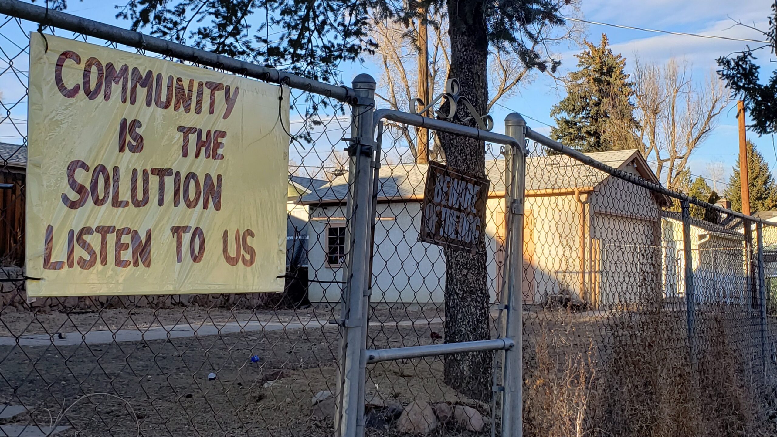 A sign on a fence reading "Community is the solution. Listen to us"