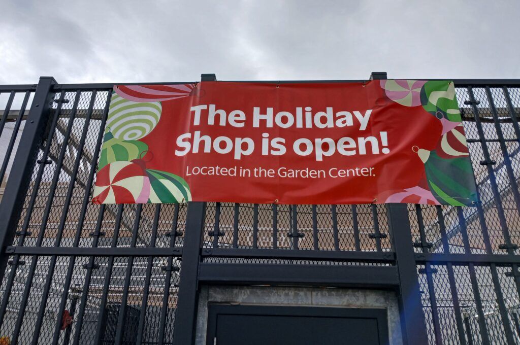 A red banner with white text in the center reading "The holiday shop is open! Located in the garden center," including cartoon holiday ornaments in various shades of red, green, pink and white, hangs outside a Walmart in Falcon, Colorado.